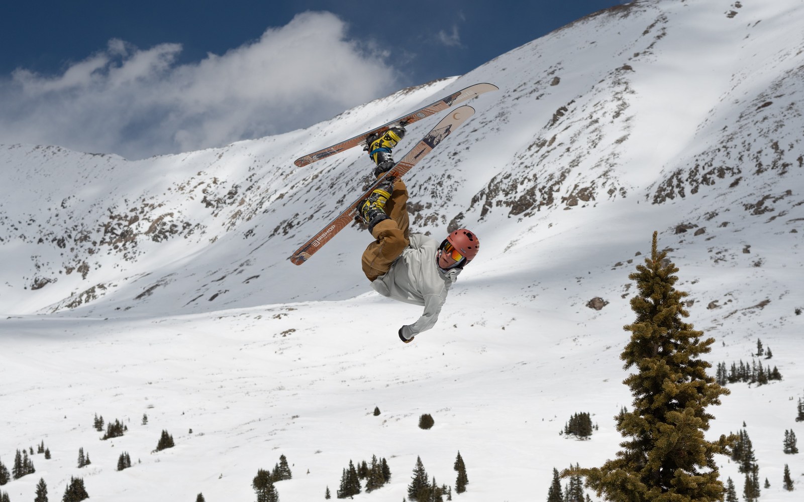 Skier performs an inverted flip on telemark skis above a snowy mountain slope