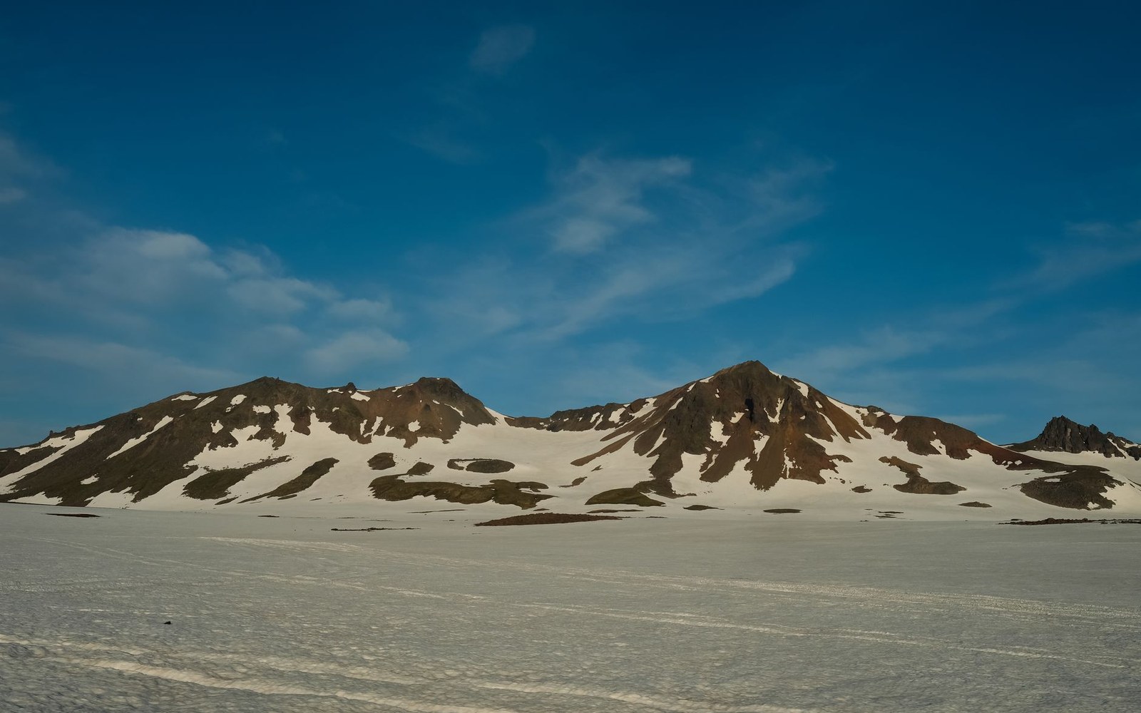Snow-covered mountain ridges with exposed rocky peaks under a clear blue sky