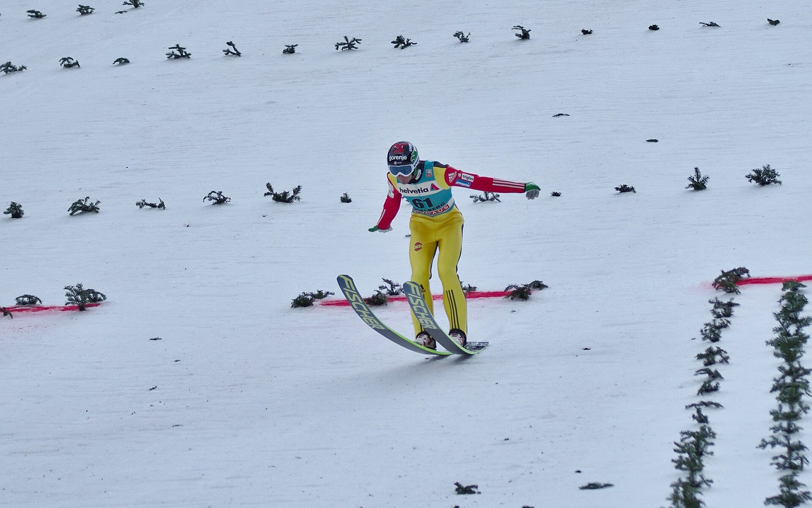 Ski jumper in yellow suit lands on the snow-covered slope, arms outstretched for balance