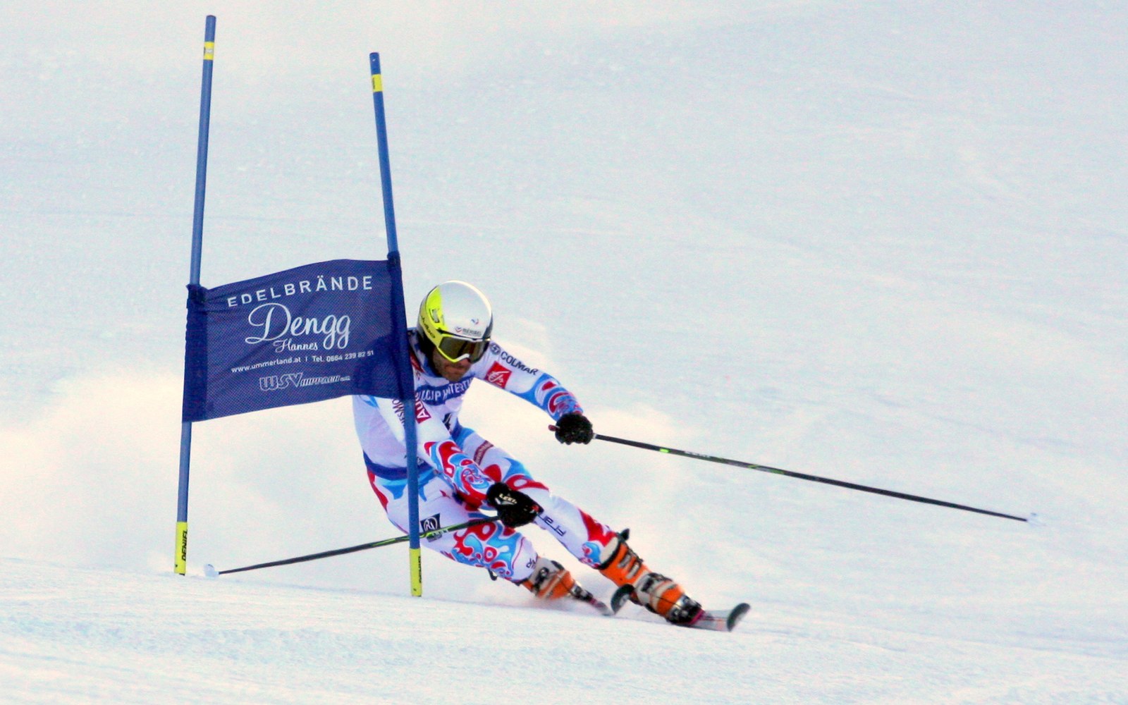 Skier in racing suit and helmet leans into a slalom gate on snow