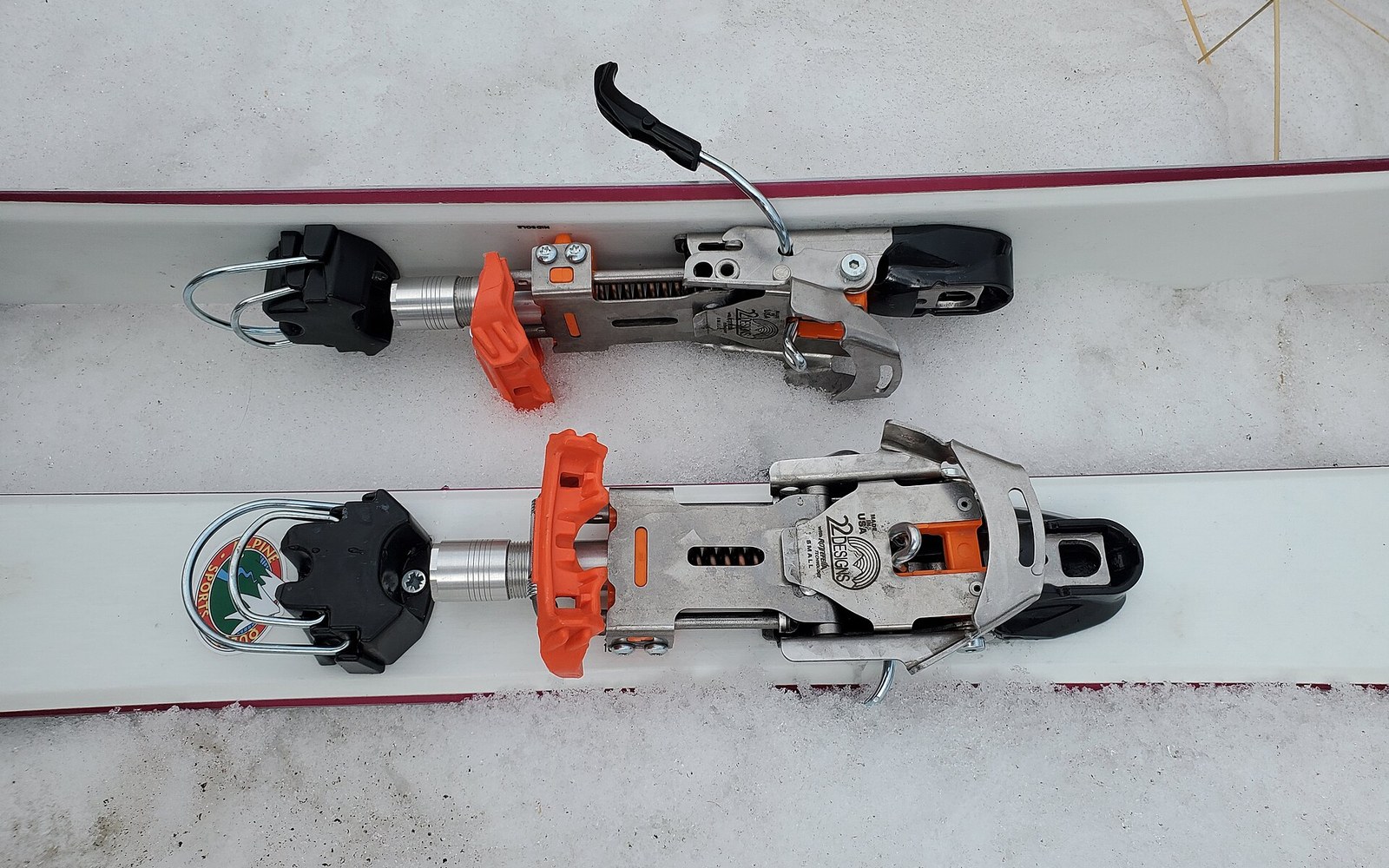 Overhead view of two telemark ski bindings with orange toe pieces mounted on skis in snow