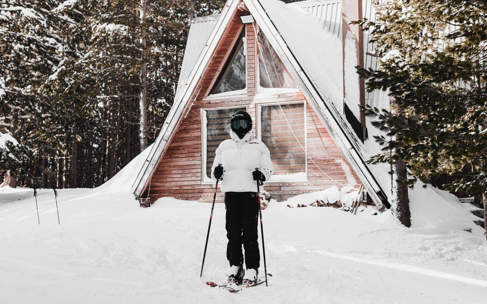 A rack of telemark skis leaning against the exterior wall of a timber ski cabin, bindings visible, grey winter light