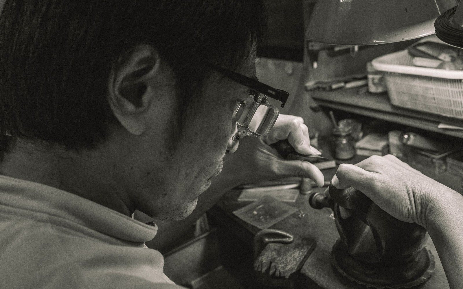 Adult hands arranging NTN binding components on a workshop bench, small metal parts organised on a cloth, a vice visible at the left edge